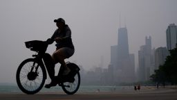A person rides a bicycle along the shore of Lake Michigan as the downtown skyline is blanketed in haze from Canadian wildfires Tuesday in Chicago. 