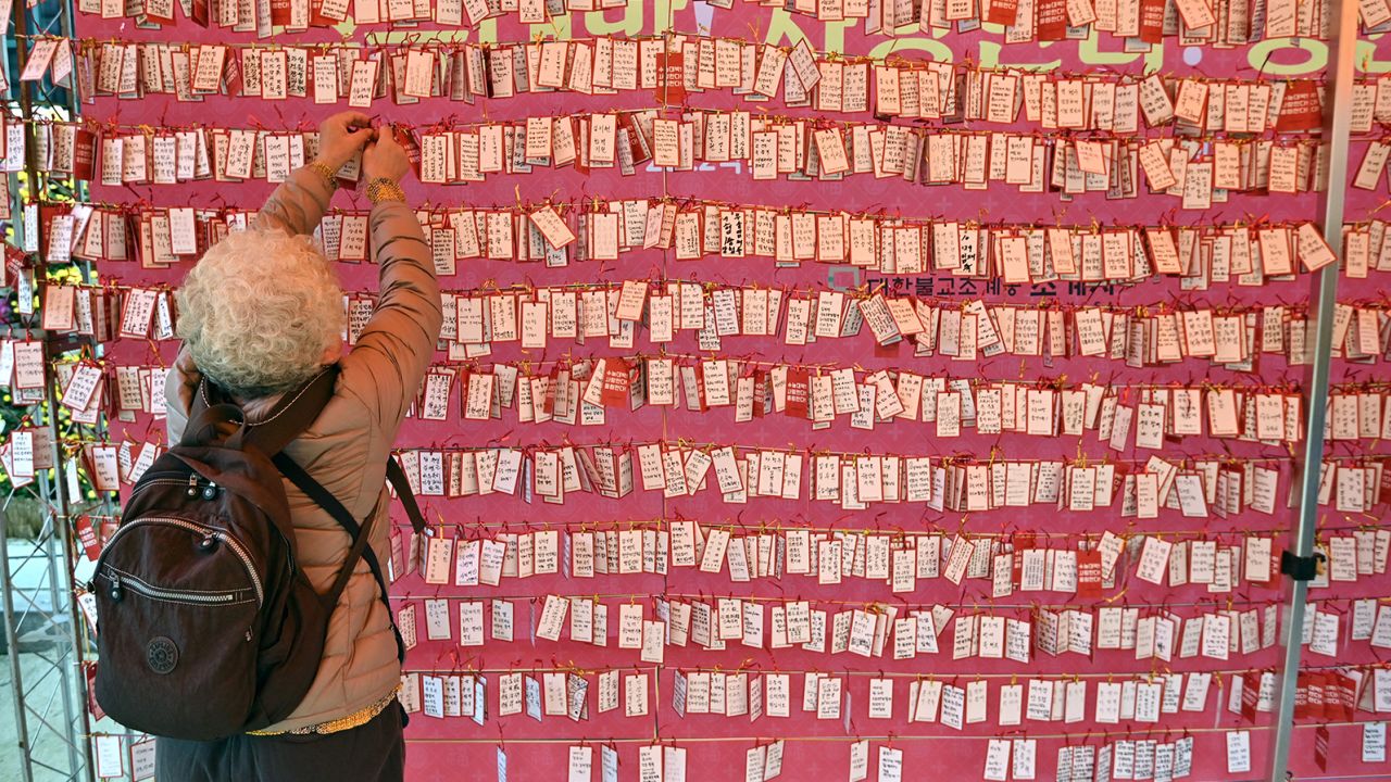 A woman attaches a name card wishing for good results for students in South Korea's college entrance exam, at a temple in Seoul on November 18, 2021. 