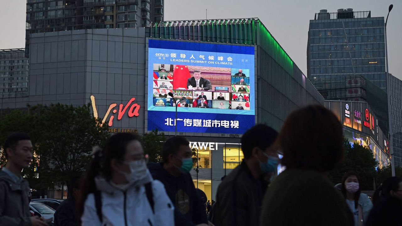 Pedestrians wait at an intersection as a news program report on Chinese President Xi Jinping's appearance at a US-led climate summit is seen on a giant screen in Beijing on April 23, 2021.