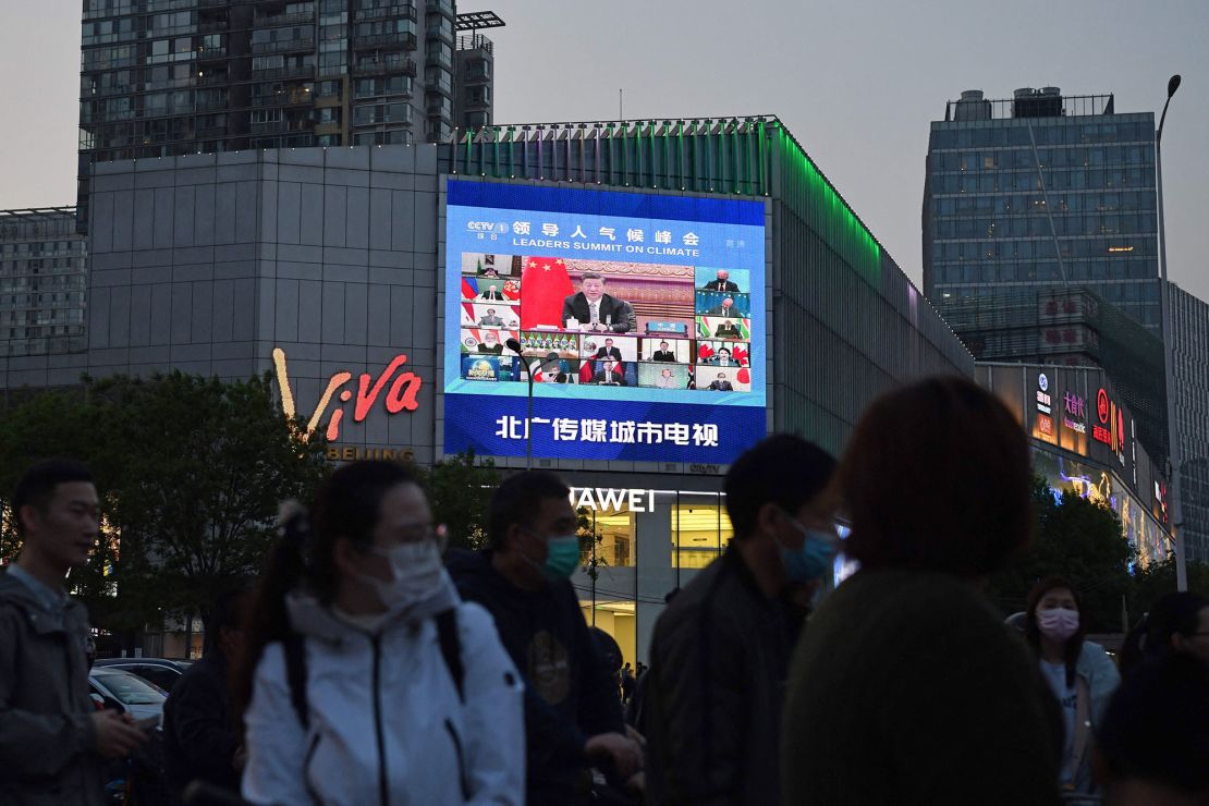 Pedestrians wait at an intersection as a news program report on Chinese President Xi Jinping's appearance at a US-led climate summit is seen on a giant screen in Beijing on April 23, 2021.