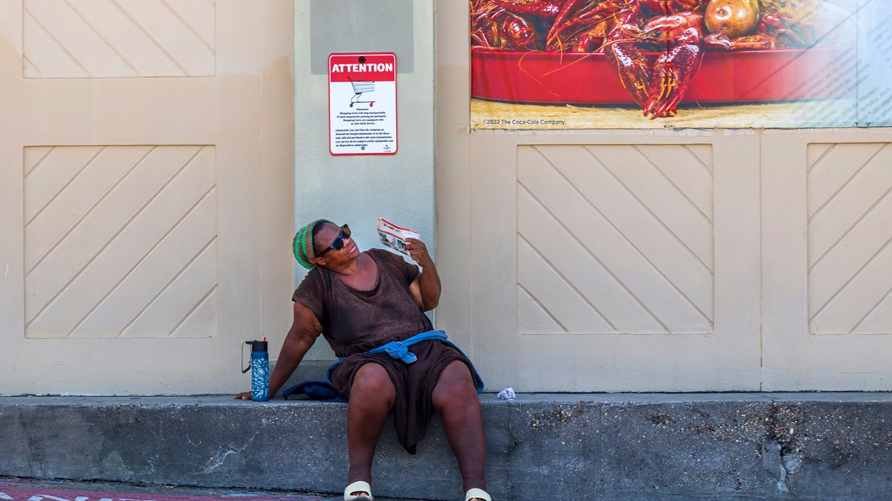 A woman fans herself underneath a hot boiled crawfish sign outside a grocery store in New Orleans, Wednesday, June 28, 2023. (Chris Granger/The Advocate via AP)