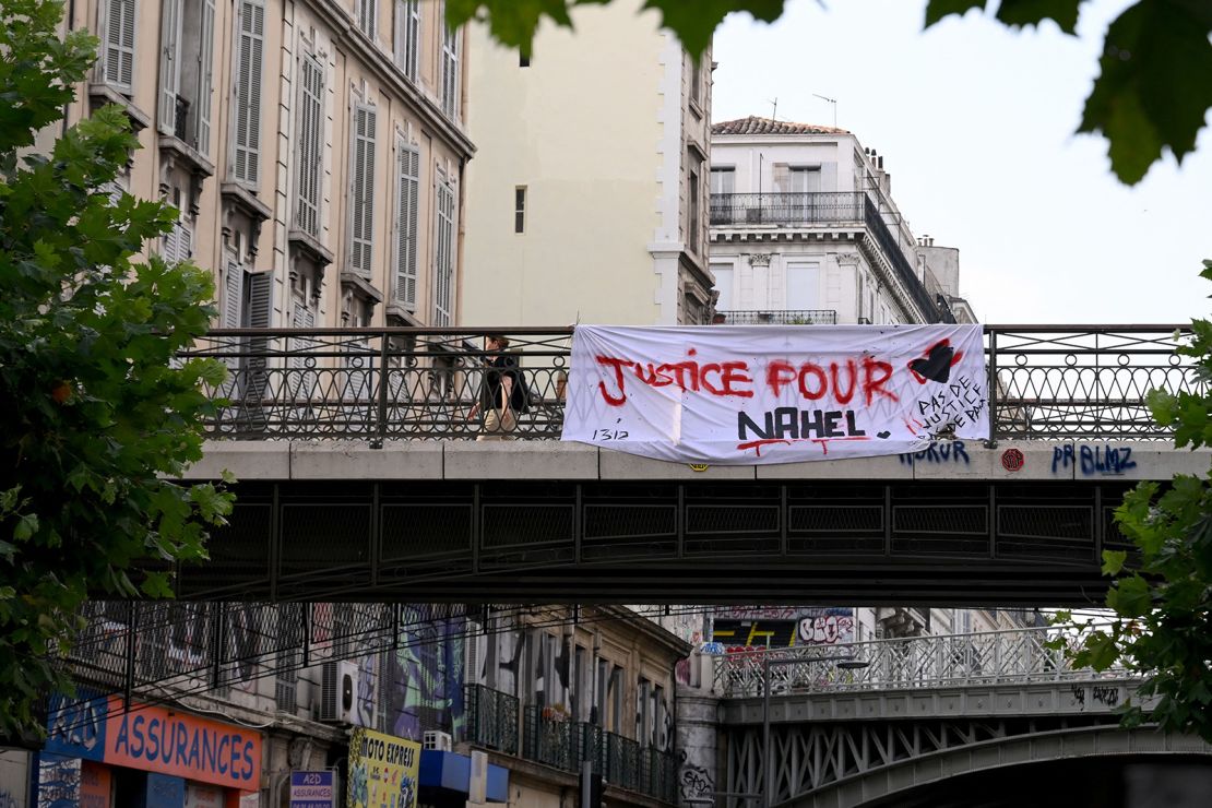 A pedestrian walks on a bridge adorned with a banner reading "Justice for Nahel" in Marseille, southern France on June 30, 2023, following the killing of teenage driver Nahel by French police in the Parisian suburb of Nanterre on June 27. French President Emmanuel Macron was scheduled to chair a new crisis meeting of ministers after a third straight night of nationwide protests over the deadly police shooting of a teenager saw cars torched, shops ransacked and hundreds arrested. (Photo by Nicolas TUCAT / AFP) (Photo by NICOLAS TUCAT/AFP via Getty Images)