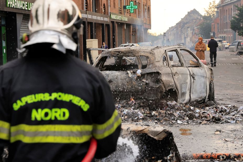 A firefighter extinguishes a car that was burnt during clashes between protesters and police in Roubaix, France, on June 30.