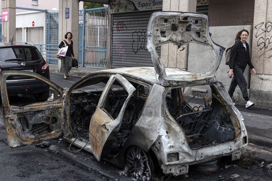 A passerby looks at the scorched remains of a car set on fire during protests on July 1, in Colombes, France.