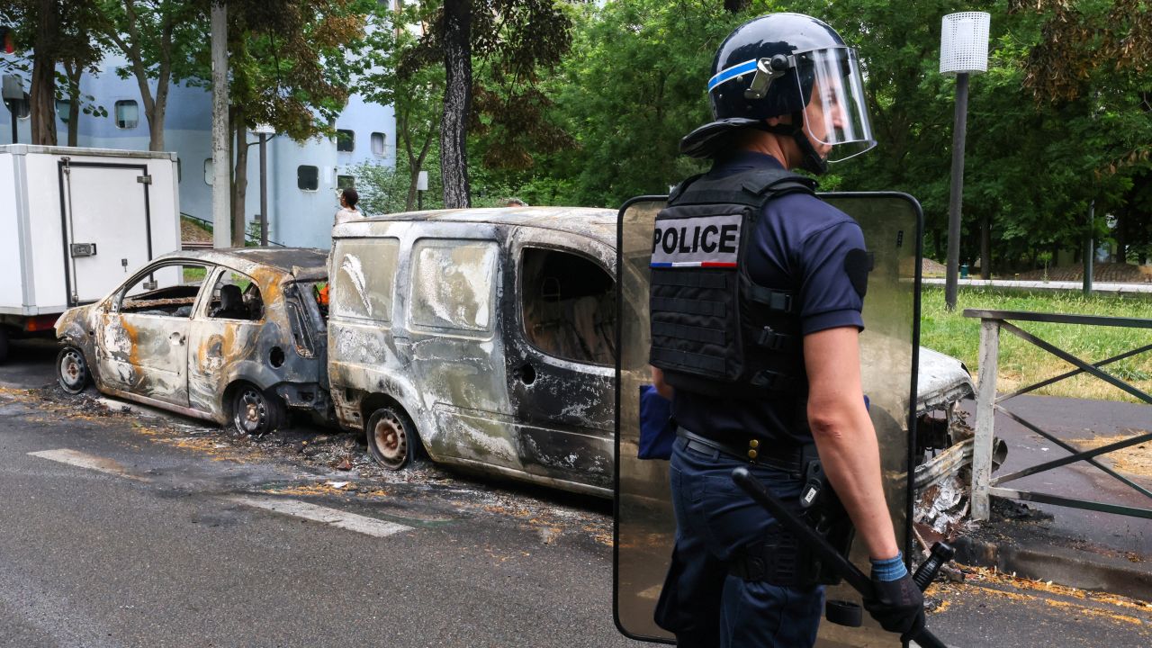 A French police officer stands guard next to vehicles burnt during a night of clashes between protesters and police, in Nanterre, Paris, on July 1, 2023. 