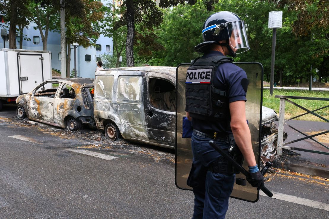 A French police officer stands guard next to vehicles burnt during a night of clashes between protesters and police, in Nanterre, Paris, on July 1, 2023. 