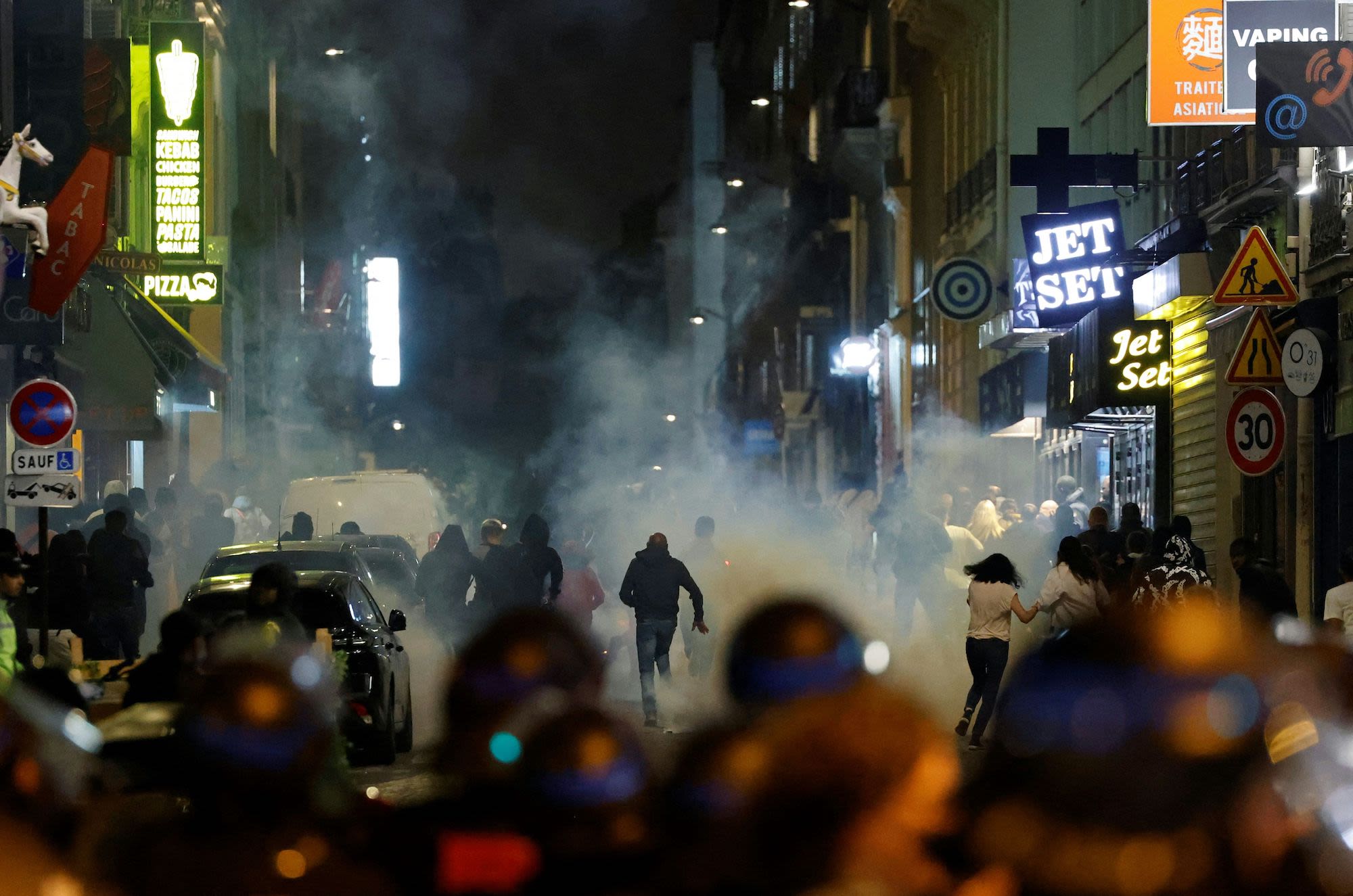 Demonstrators run as French police officers shoot tear gas in Paris on July 2.