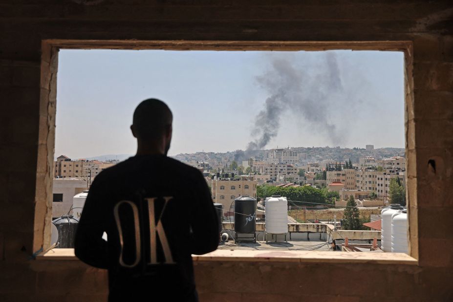 A Palestinian man looks out the window Monday as smoke billows following an Israeli airstrike in Jenin.
