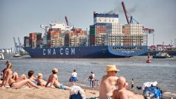 10 June 2023, Hamburg: People enjoying the sun on the Elbe beach at Övelgönne while the container ship "CMA GM Carl Antoine" sails upstream in the background. Photo: Georg Wendt/dpa (Photo by Georg Wendt/picture alliance via Getty Images)
