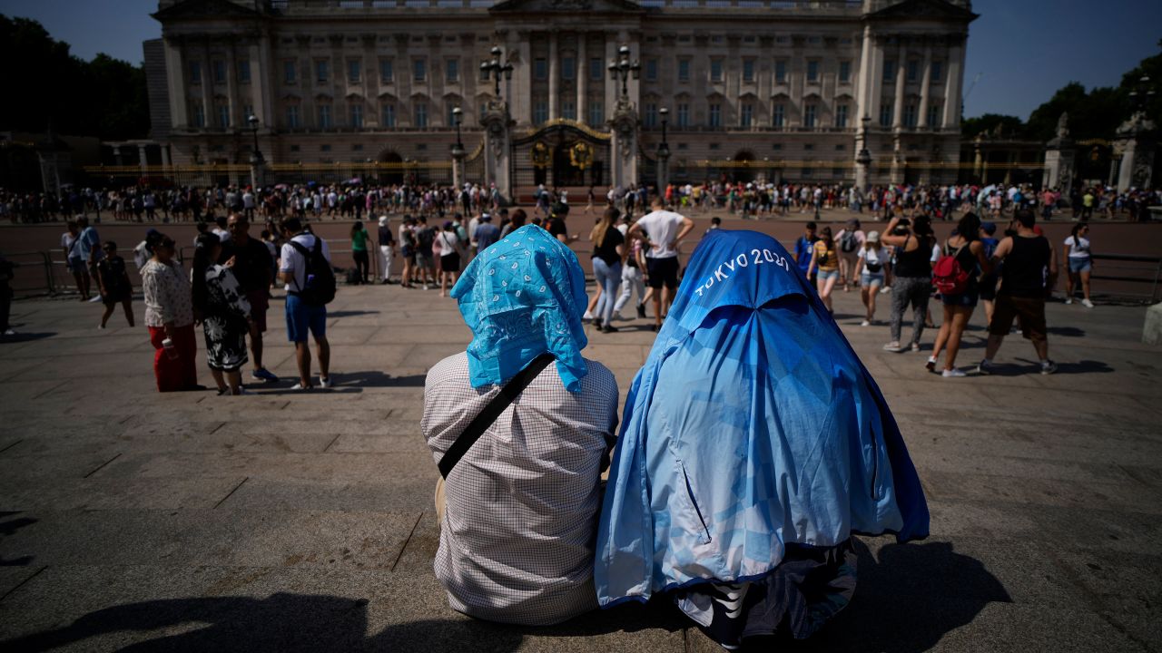 People sit covering their heads from the sun after a scaled down version of the Changing of the Guard ceremony took place outside Buckingham Palace, during hot weather in London, Monday, July 18, 2022. 