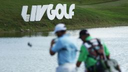 DORAL, FLORIDA - OCTOBER 30: A golfer and caddie walk by LIV Golf signage during the team championship stroke-play round of the LIV Golf Invitational - Miami at Trump National Doral Miami on October 30, 2022 in Doral, Florida.