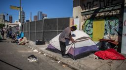 A homeless man zips up his tent in front of the non-profit Midnight Mission's headquarters, while traditional Thanksgiving meals are served to nearly 2000 homeless people in the Skid Row neighborhood of downtown Los Angeles on November 25, 2021. (Photo by Apu GOMES / AFP) (Photo by APU GOMES/AFP via Getty Images)