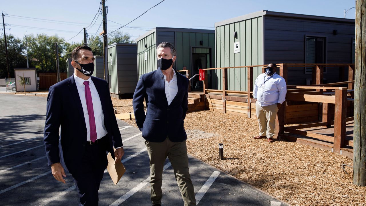 El gobernador de California, Gavin Newsom, al centro, y el alcalde de San José, Sam Liccardo, a la izquierda, recorren un sitio comunitario de viviendas de emergencia en San José en octubre de 2020, poco después de que Newsom anunciara más fondos para combatir la falta de vivienda.