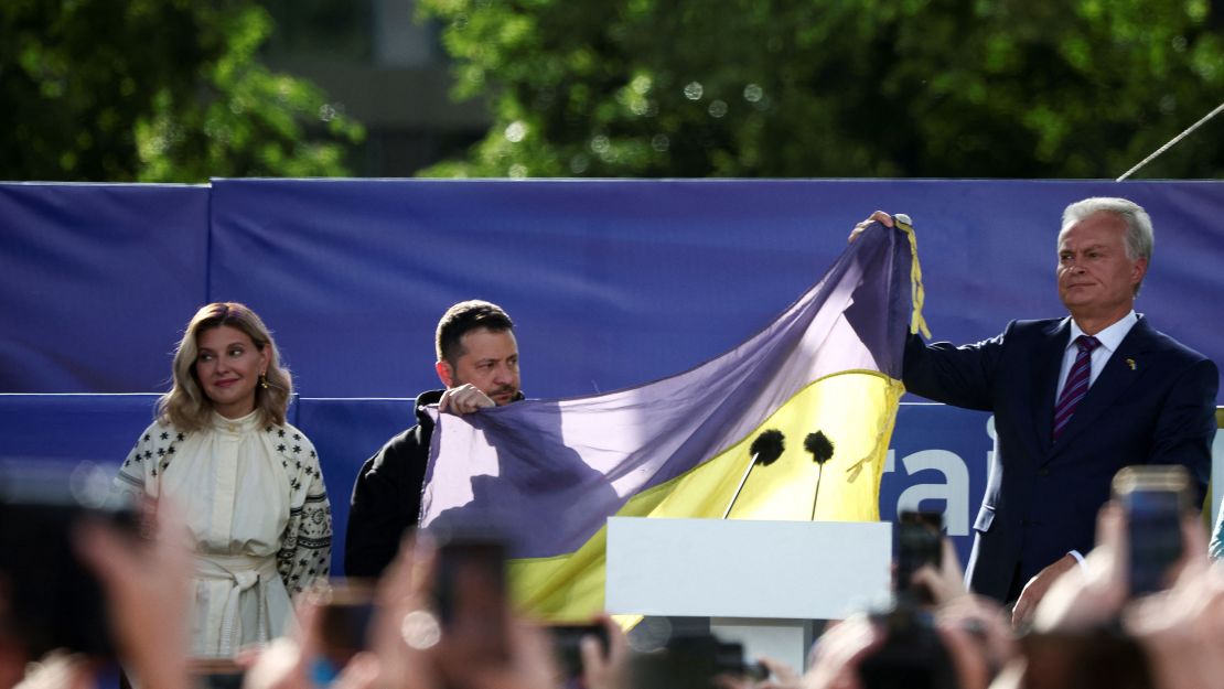 Ukrainian President Volodymyr Zelensky and Lithuanian President Gitanas Nauseda hold a Ukrainian flag from the front line of the war with Russia, next to Olena Zelenska, in Vilnius on July 11, 2023.