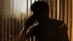 Silhouette of an unknown man on a phone against window blinds. Conceptual with space for copy.