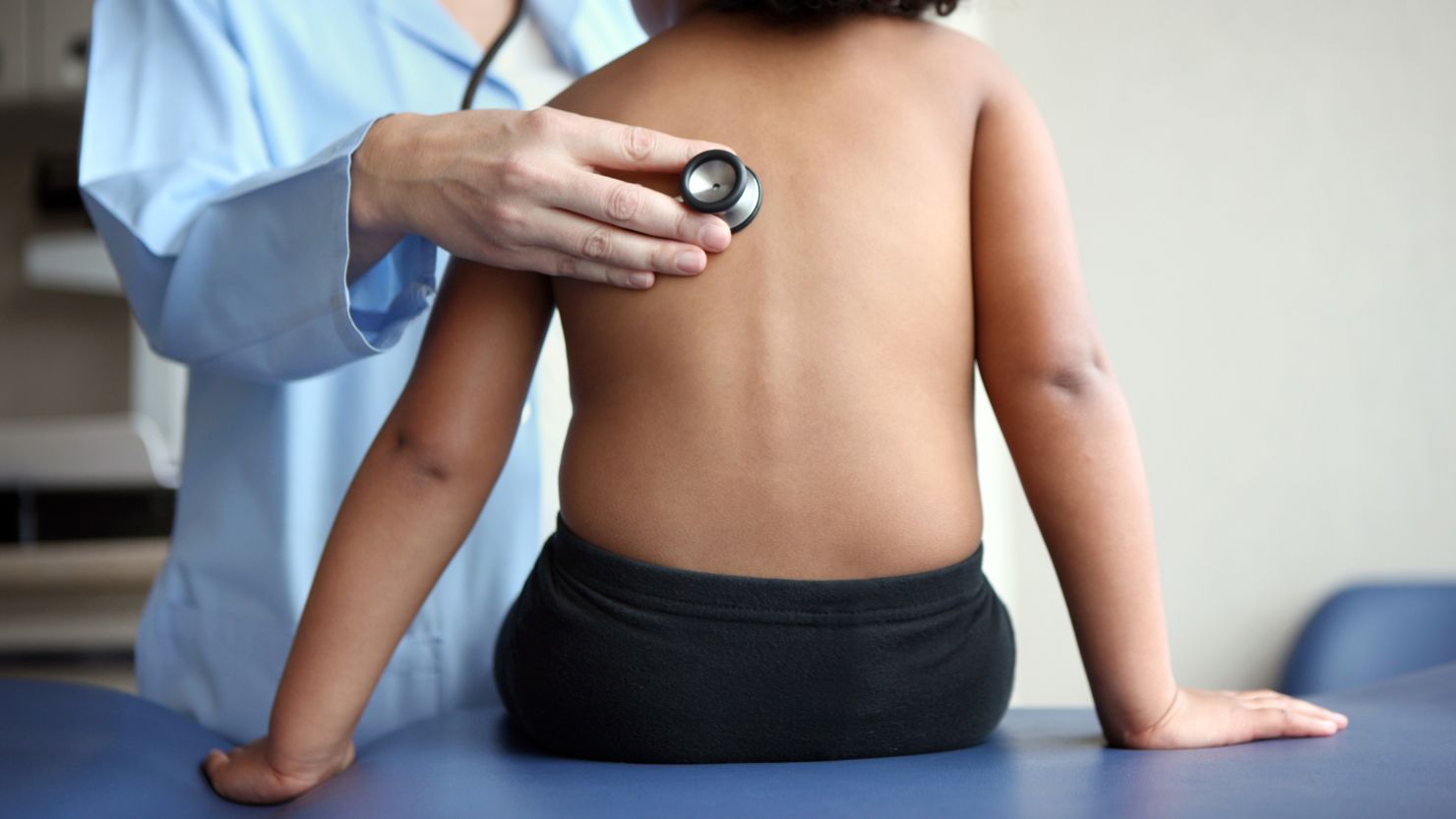 A female pediatrician listens to a three-year-old girl's lungs with a stethoscope.