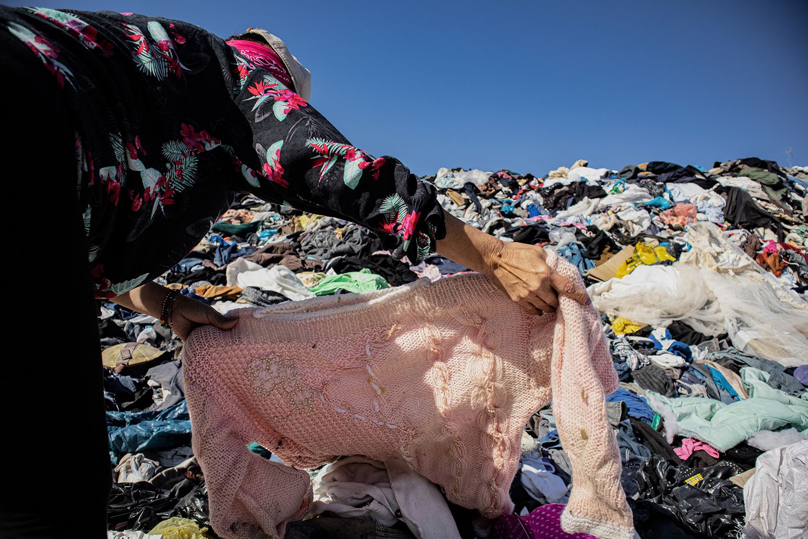 25 November 2021, Chile, Alto Hospicio: A woman searches for an item of clothing among a mountain of used clothes at a garbage dump. In the nearby free trade zone of Iquique, 29,178 tons of used clothing arrived in 2021 through October. About 50 importers sell the best pieces from them, while the others - estimated at 40 percent - sort them out. (to dpa "Chile's Atacama Desert: Graveyard for Used Clothes") Photo: Antonio Cossio/dpa (Photo by Antonio Cossio/picture alliance via Getty Images)