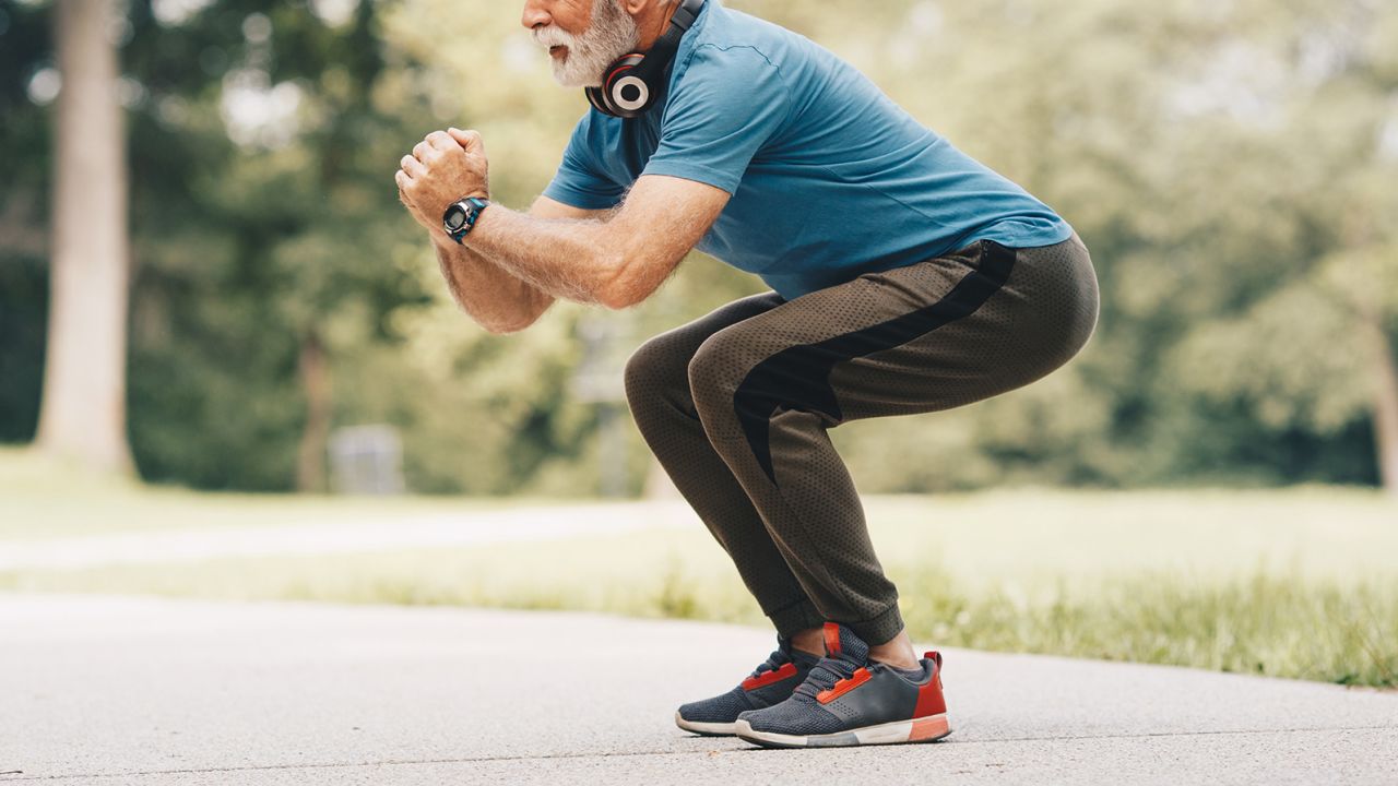 Active senior is in park, on treadmill, doing exercises. He enjoys in nature, fresh air and lovely sunny spring day. After series of stretching and warming up, he started do do squats.