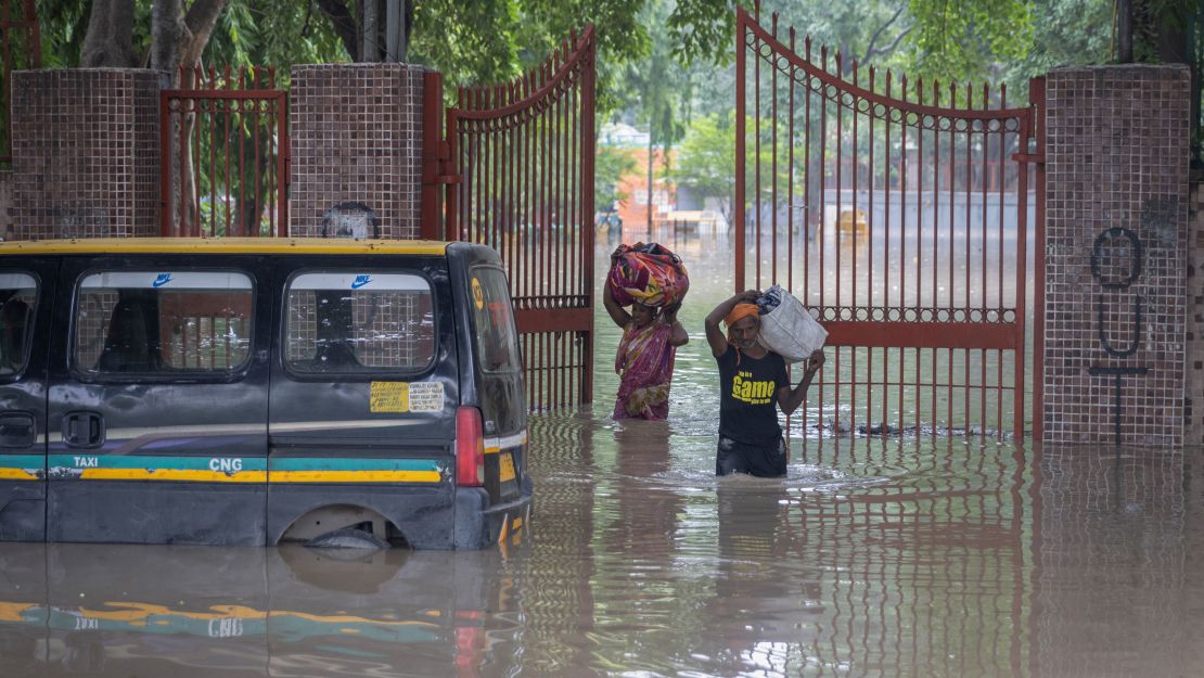 A couple carries their belongings as they leave a flooded cremation ground in New Delhi on July 13, 2023.