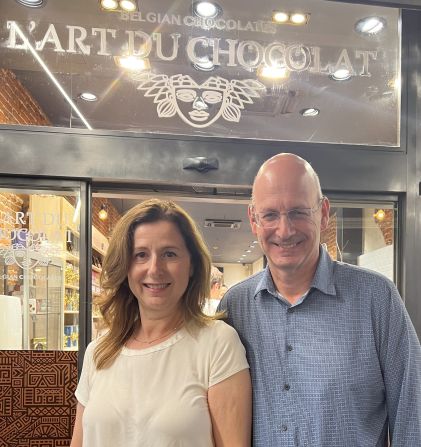 <strong>Revisiting the past:</strong> Here's the couple pictured in June 2023 on a visit to Brussels, outside the chocolate shop where they first met. "I find it amazing and lucky that our meeting at the chocolate shop led to our dates and romance and later relationship," says Myriam. "You never know where you might meet the love of your life."