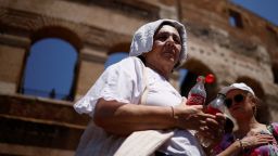 A woman queues to fill bottles with water near the Colosseum as she shelters from the sun with a towel during a heatwave across Italy, in Rome, July 11, 2023. REUTERS/Guglielmo Mangiapne