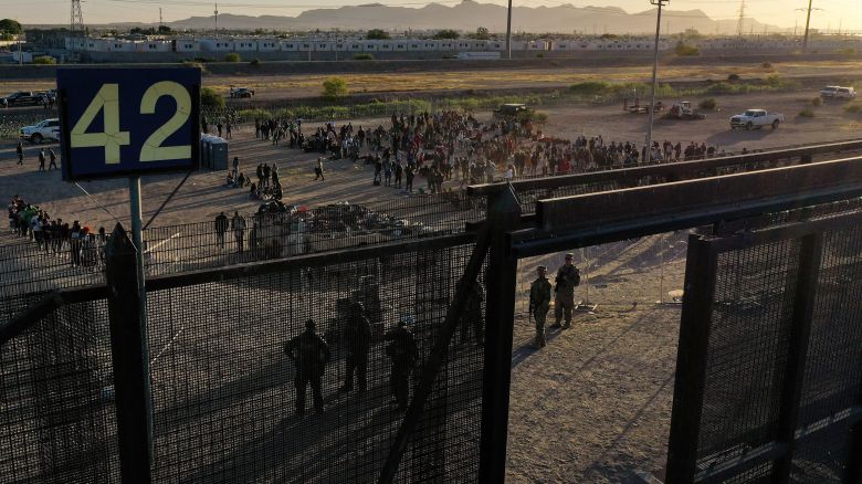 TOPSHOT - In this aerial picture taken on May 11, 2023 migrants line up to walk through gate 42 to board vans after waiting along the border wall to surrender to US Customs and Border Protection (CBP) Border Patrol agents for immigration and asylum claim processing upon crossing the Rio Grande river into the United Staes on the US-Mexico border in El Paso, Texas. The US on May 11, 2023, will officially end its 40-month Covid-19 emergency, also discarding the Title 42 law, a tool that has been used to prevent millions of migrants from entering the country. (Photo by Patrick T. Fallon / AFP) (Photo by PATRICK T. FALLON/AFP via Getty Images)