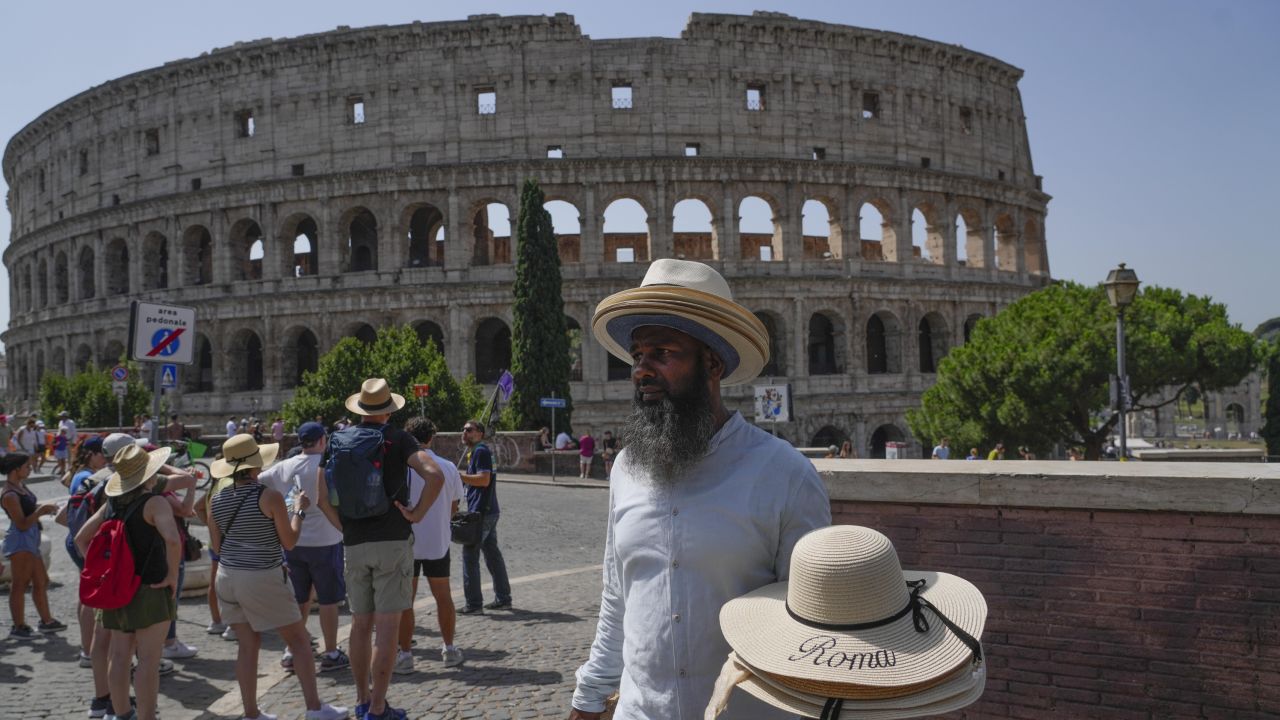 A street vendor walks with hats in front of the Colosseum in Rome, Monday, July 17, 2023.