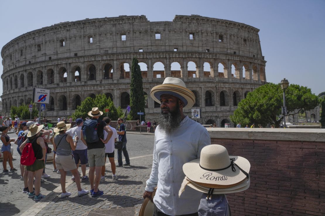 A street vendor walks with hats in front of the Colosseum in Rome, Monday, July 17, 2023.