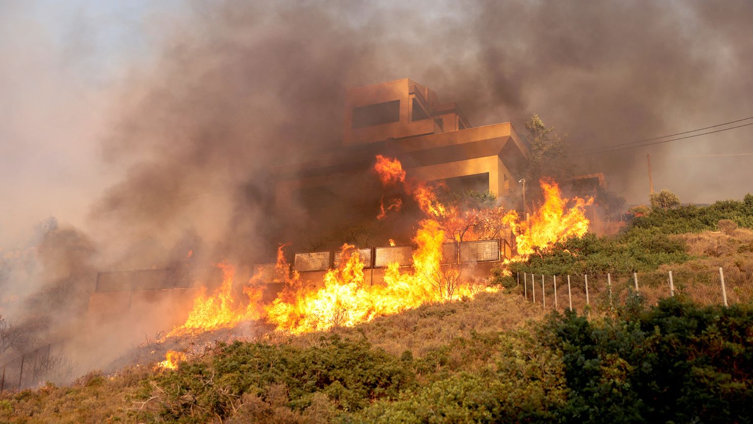 Flames engulf a house as a wildfire burns in Saronida, near Athens, Greece, on Monday.