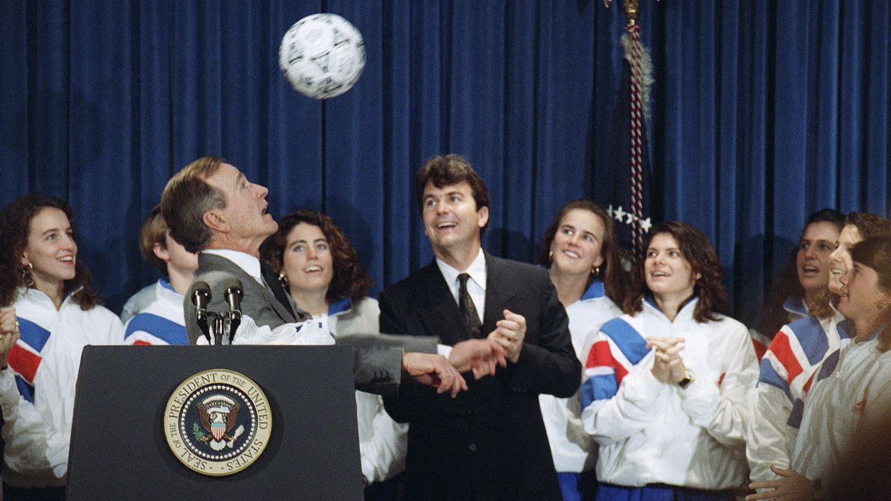President George Bush heads a soccer ball while meeting the 1991 Women's World Cup soccer champs, Jan. 23, 1992 in Washington. Anson Dorrance, coach of the team looks on at right. (AP Photo/Barry Thumma)