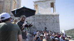 A tour guide uses an umbrella and gloves to shield himself from the sun with while touring the Acropolis archaeological site, during extreme hot weather conditions, in Athens, Greece.