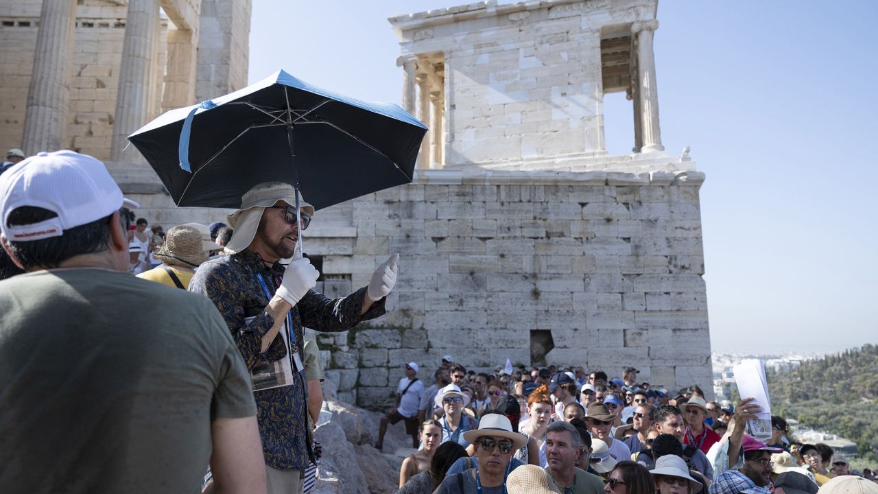 A tour guide uses an umbrella and gloves to shield himself from the sun while working at the Acropolis archaeological site during extreme hot weather in Athens, Greece.