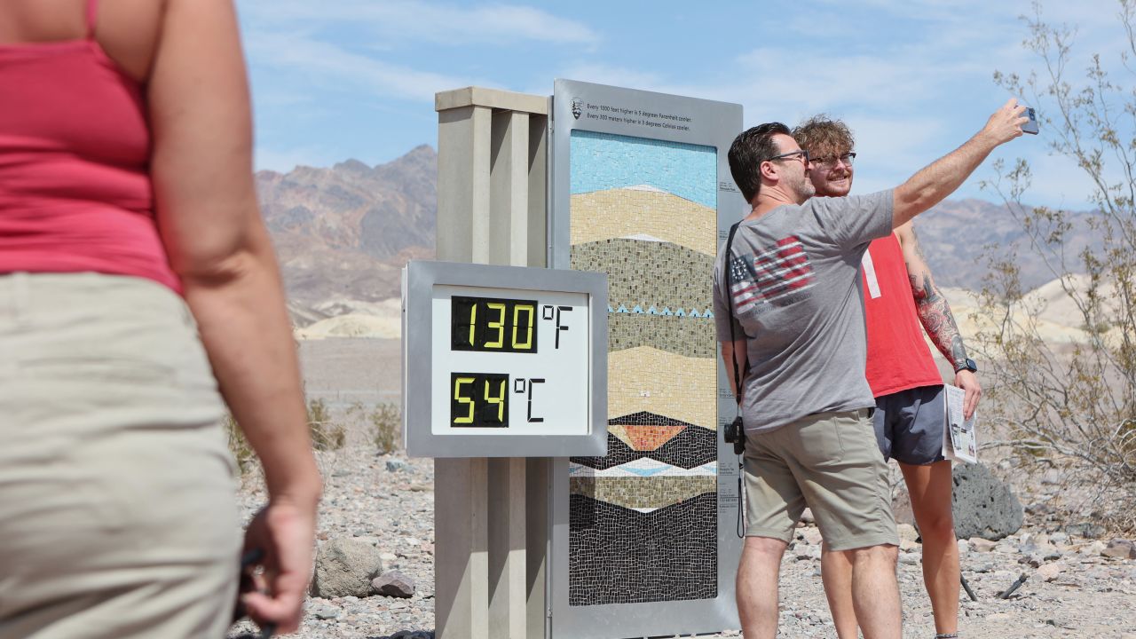 Tourists stand next to an unofficial heat reading at Furnace Creek Visitor Center during a heat wave in Death Valley National Park.