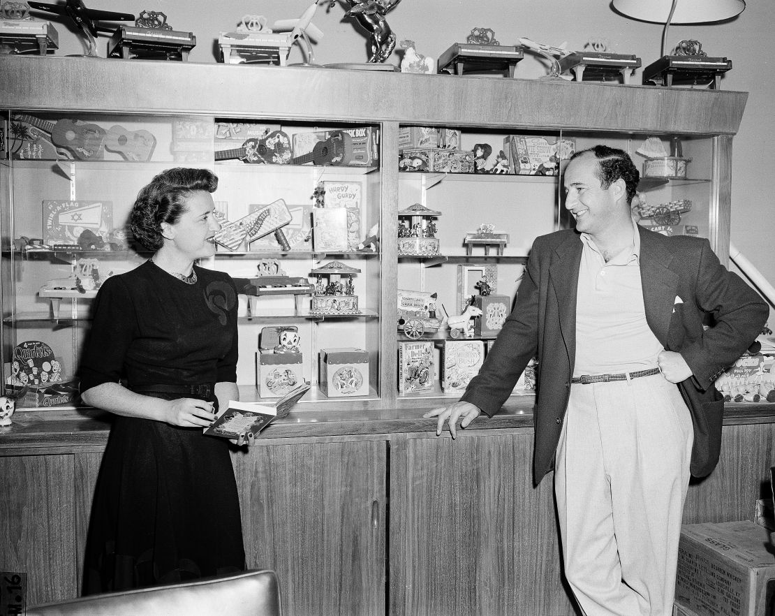 Ruth and Elliot Handler, pose before display case in their office showing toys they have developed in 1951.