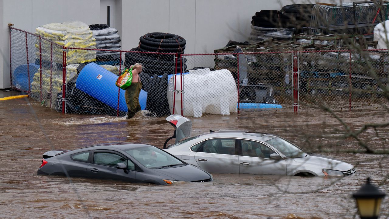 A man wearing chest waders walks past cars abandoned in floodwaters in a mall parking lot in Halifax, Nova Scotia, on Saturday.