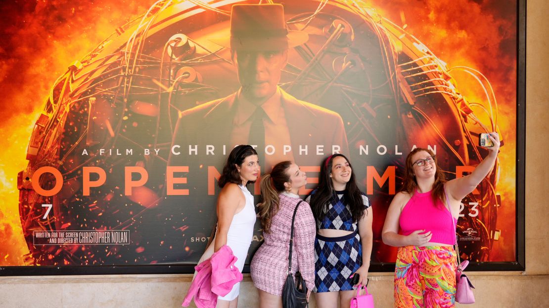 From left, Gabrielle Roitman, Kayla Seffing, Maddy Hiller and Casey Myer take a selfie in front of an "Oppenheimer" movie poster before attending an advance screening of "Barbie," on July 20, 2023, at AMC The Grove 14 theaters in Los Angeles.