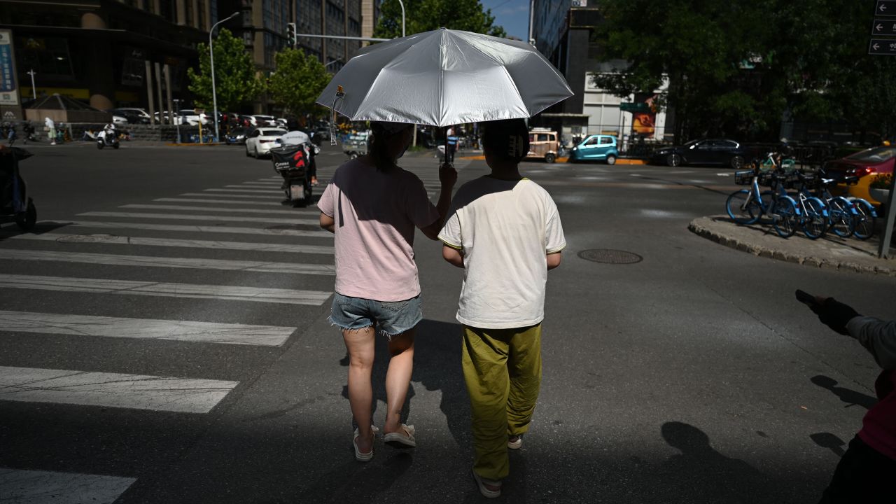 People shelter from the sun as they cross a road during a heatwave in Beijing on July 7, 2023.