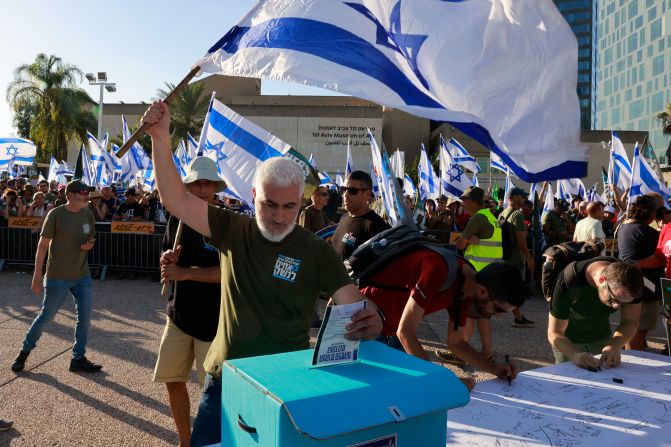 An Israeli military reservist in Tel Aviv waves a national flag as he drops a signed declaration in a box, announcing the suspension of his voluntary reserve duty, on Wednesday, July 19. He was protesting the government's judicial overhaul plans.