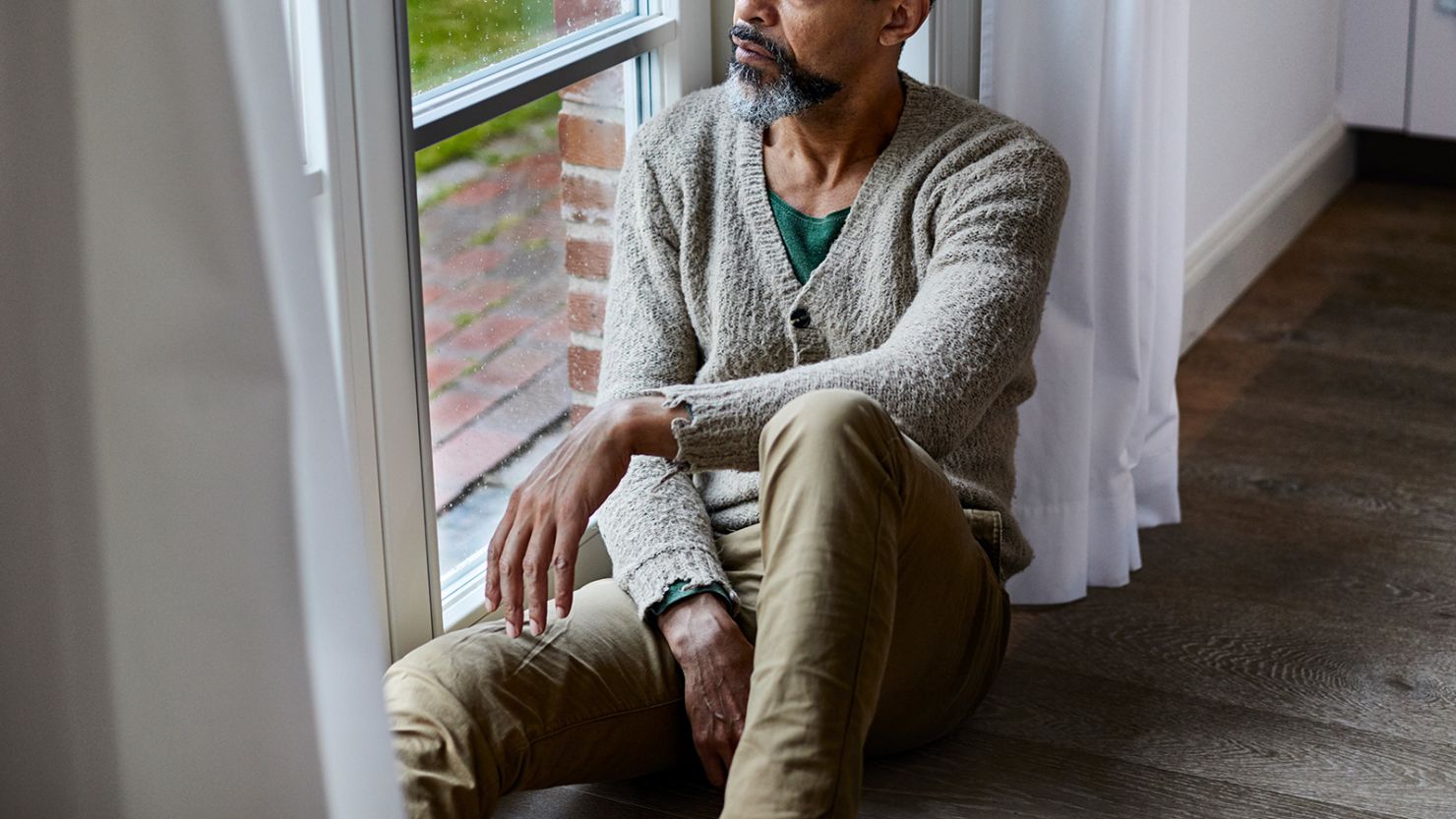 Pensive man sitting on the floor looking out of window