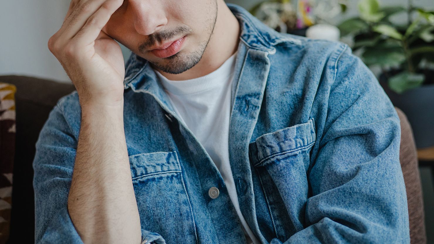 A sad young man in the living room. He suffers from depression