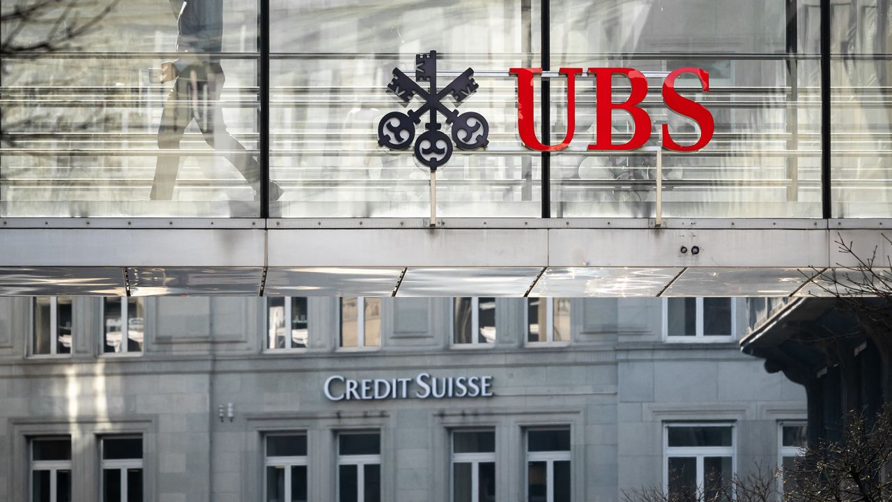 A employee is seen in silhouette with sign of Swiss giant banking UBS and a sign of Credit Suisse bank in Zurich on March 20, 2023. 
