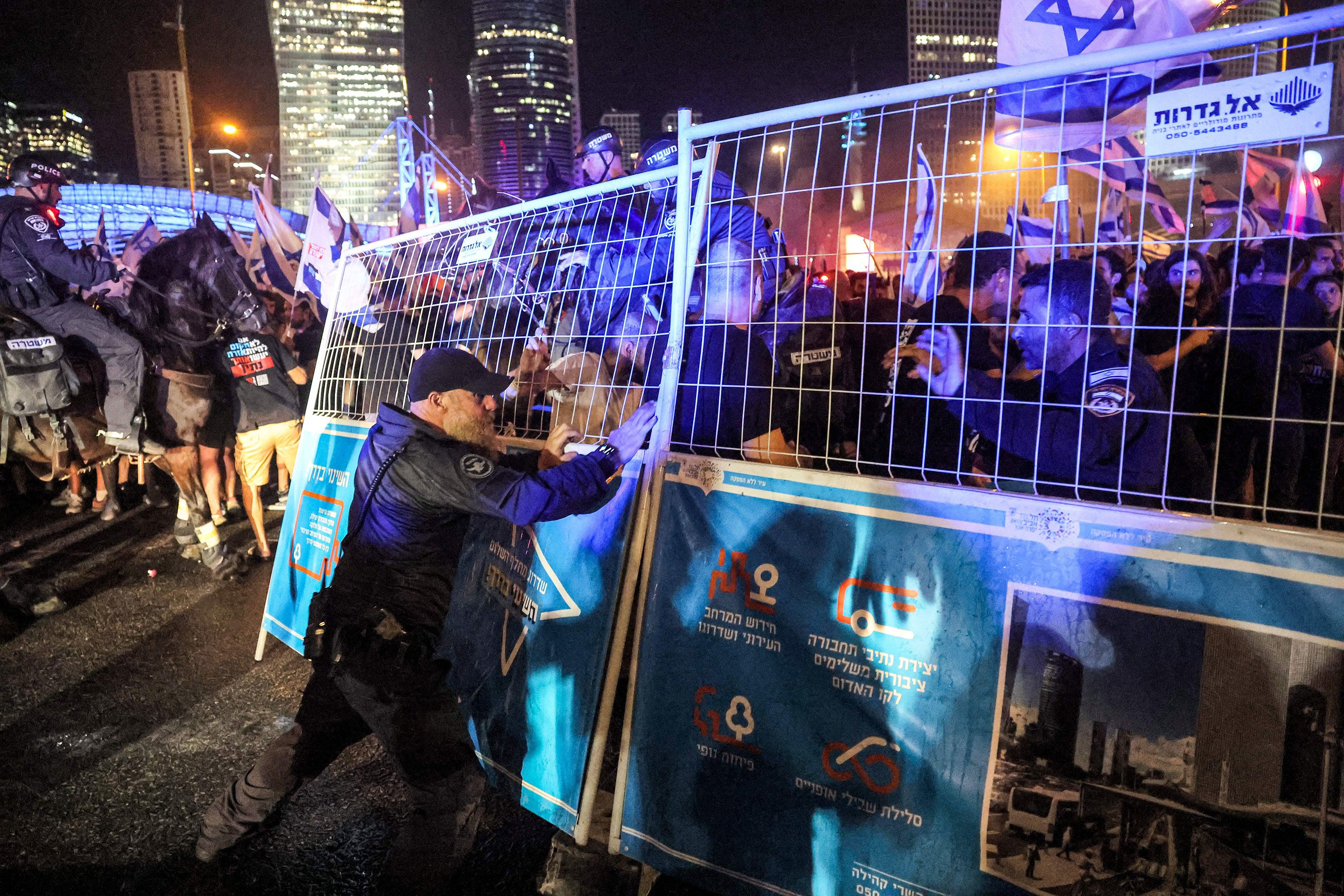 An Israeli policeman stands behind a metal fence being shoved by demonstrators in Tel Aviv on July 24.