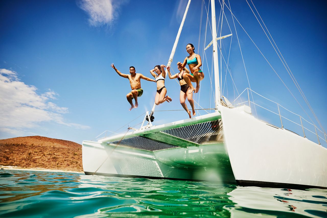 Wide shot of friends jumping into the ocean from the deck of sailboat while on vacation.