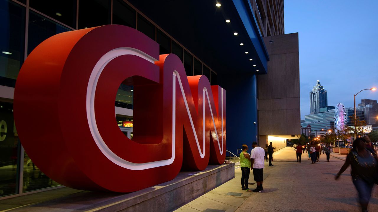 Pedestrians pass in front of CNN signage displayed at the network's headquarters building in Atlanta, Georgia, U.S., on Saturday, Aug. 2, 2014.