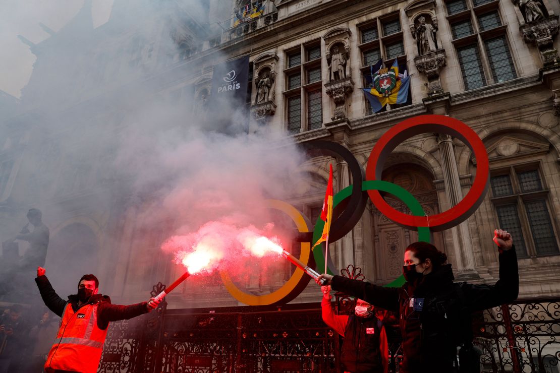 Protestors light red flares in front of the Olympic rings in Paris.