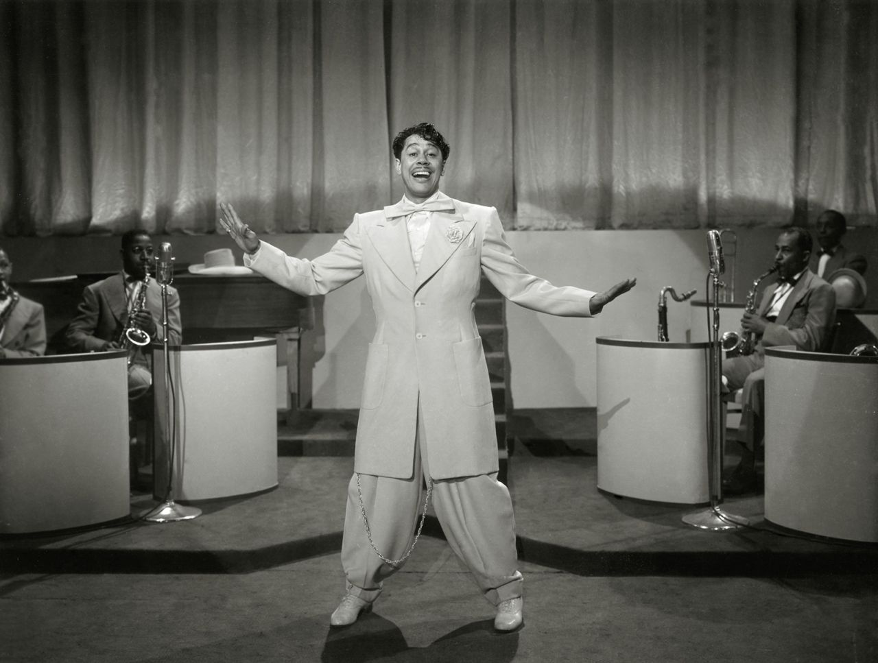 Cab Calloway performs in the 1943 movie "Stormy Weather," wearing a supersized zoot suit — a knee-length coat jacket, bow tie and billowing wide-leg pants.