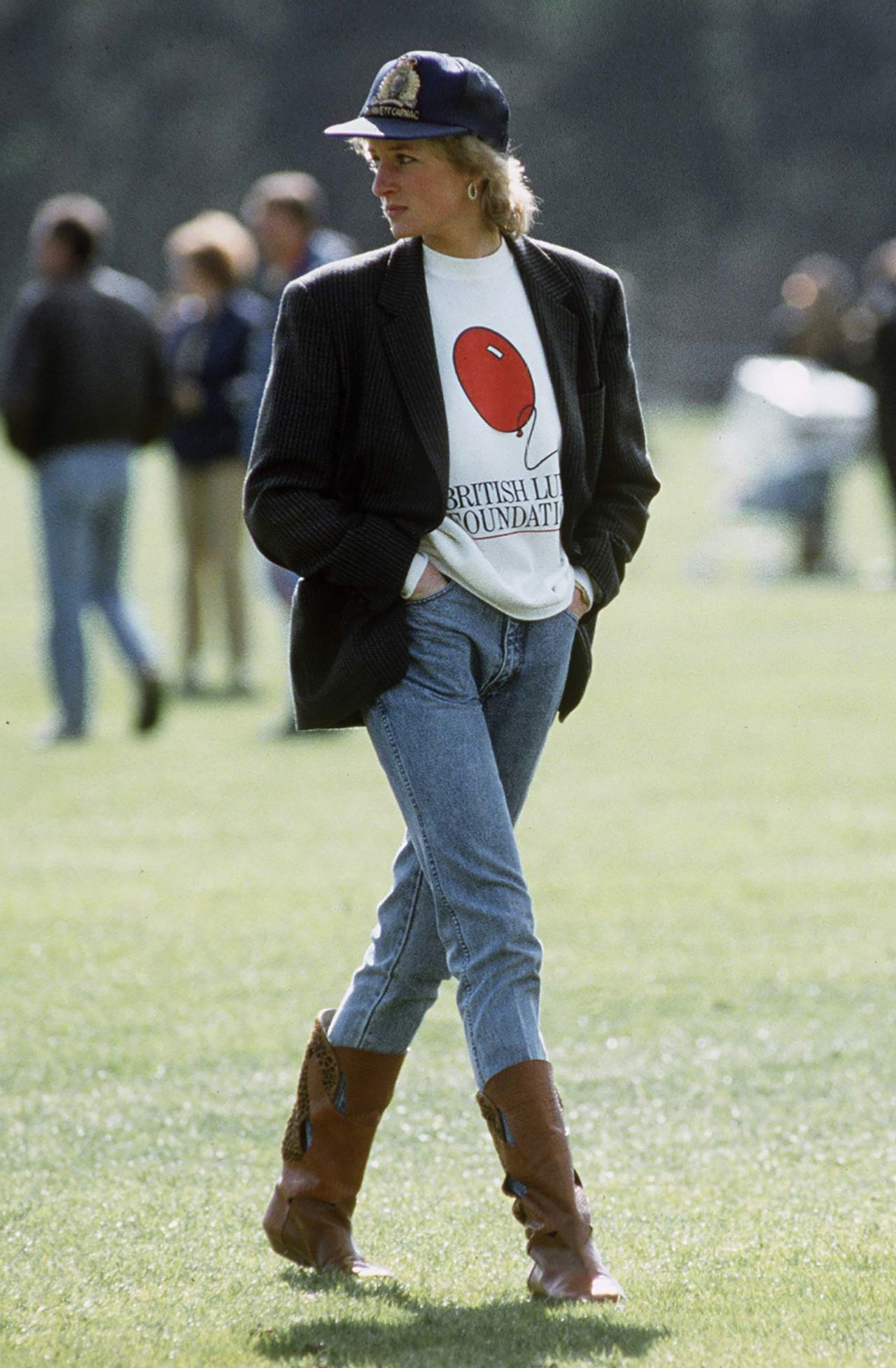 Princess Diana is pictured attending a game at the Guards Polo Club in Windsor, England. In an outfit that defined her style in the 1980s, she is dressed casually in a sweatshirt with The British Lung Foundation's logo under a boxy corduroy jacket and paired with jeans, boots and a baseball cap.