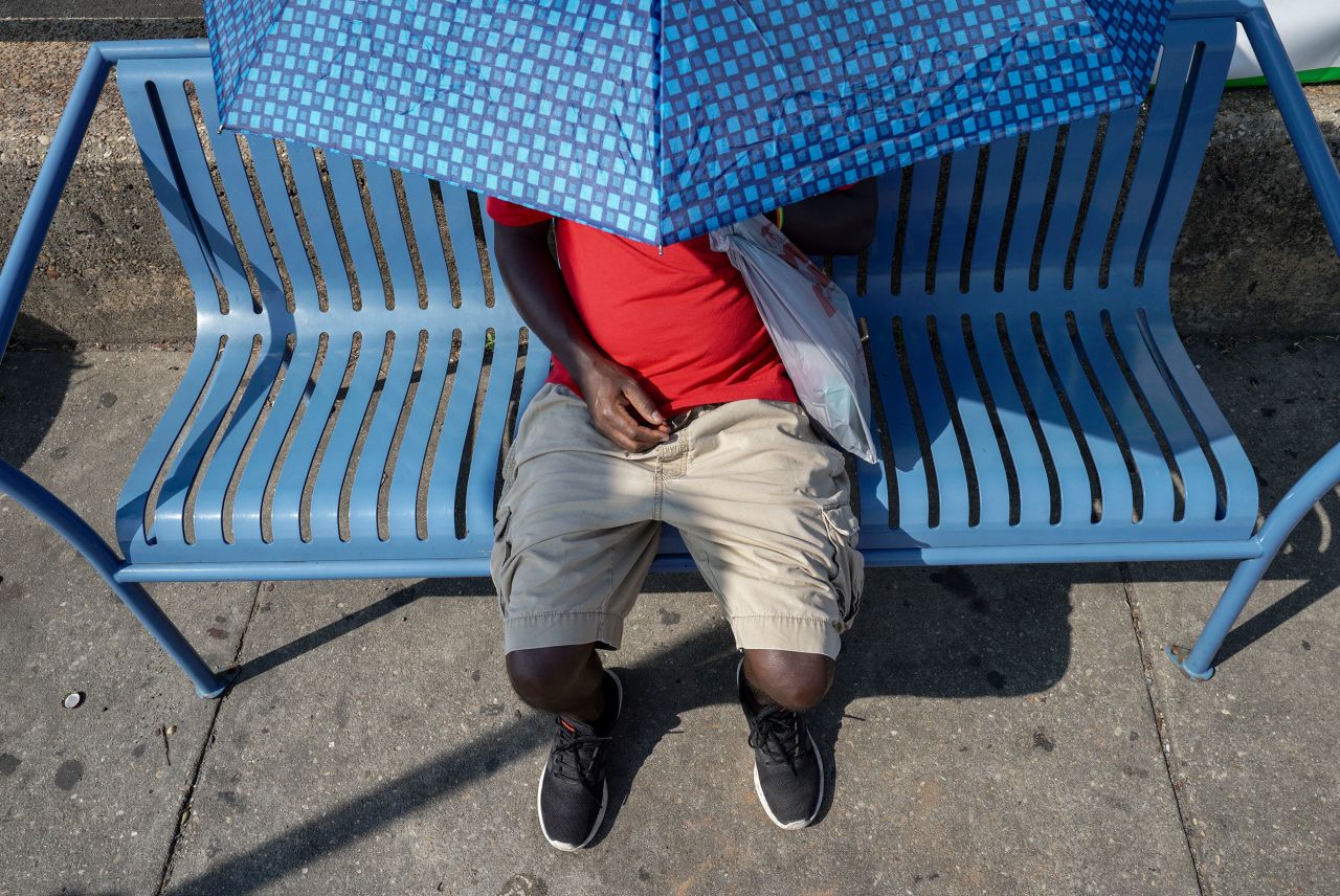 Yemichael Abebe uses an umbrella to take shelter from the sun while waiting for a bus in Takoma Park, Maryland, on July 27.