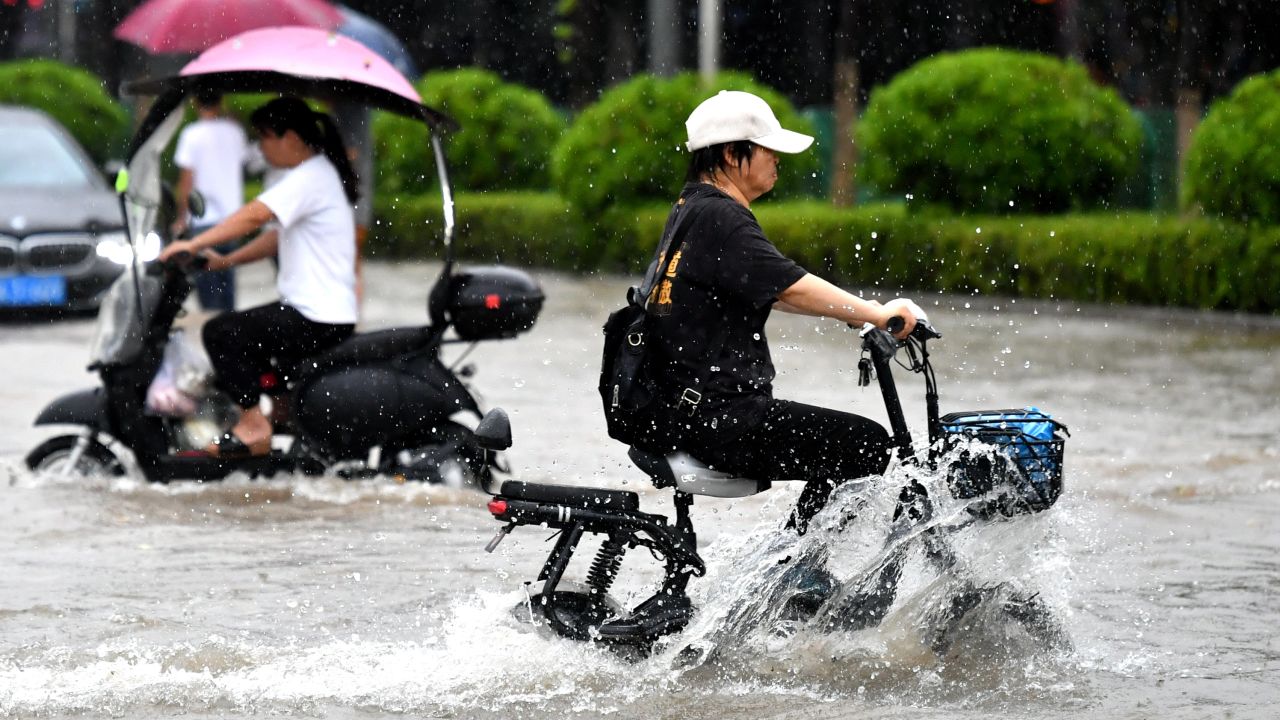  Велосипедисти карат по наводнена улица във Фуджоу. class=