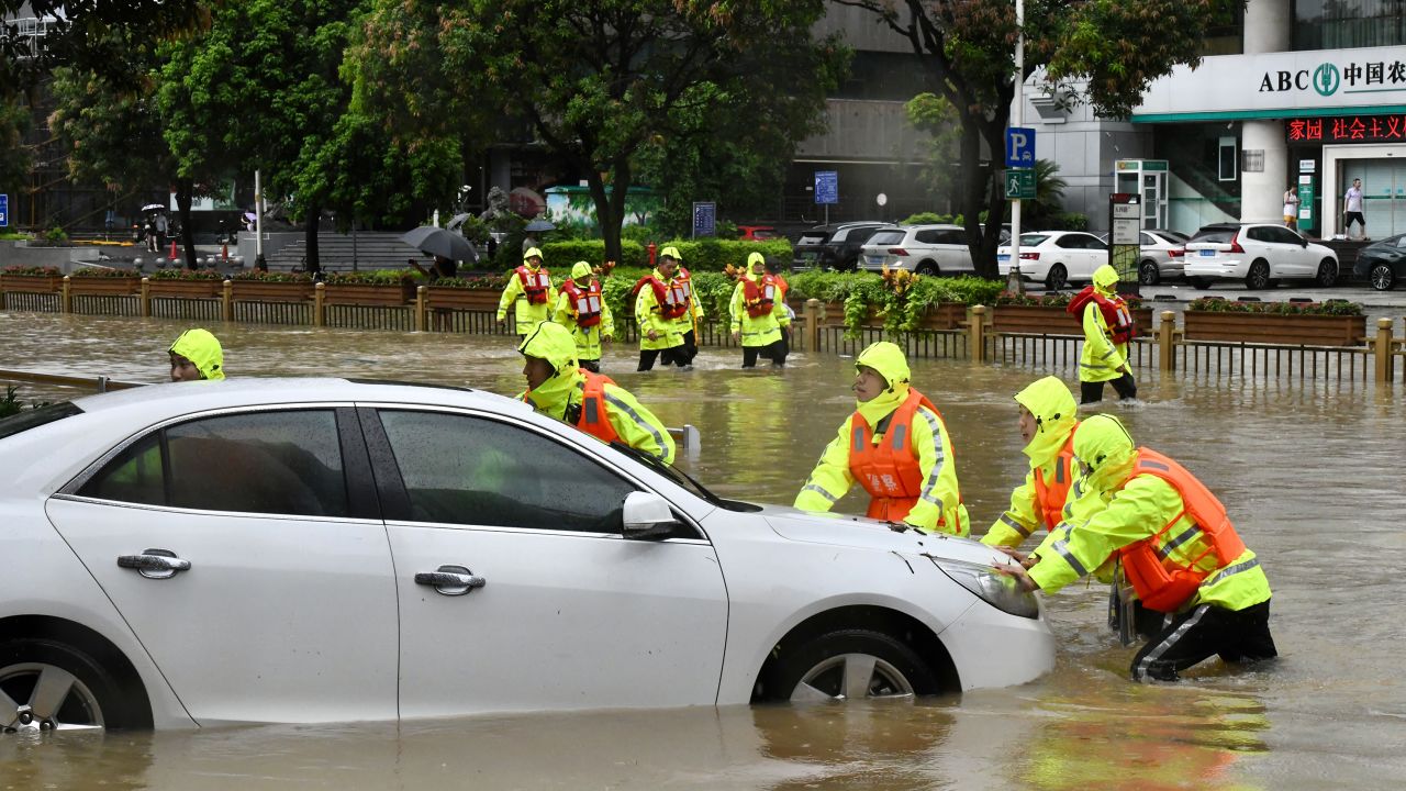 Rescuers push a trapped car in a flooded street.